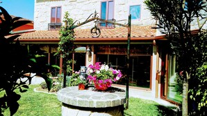 A building with a stone facade, a tiled roof, and a circular stone fountain with flowers. - Beautiful house with porch and garden 5' drive from the beach and the mountains. (Moaña)