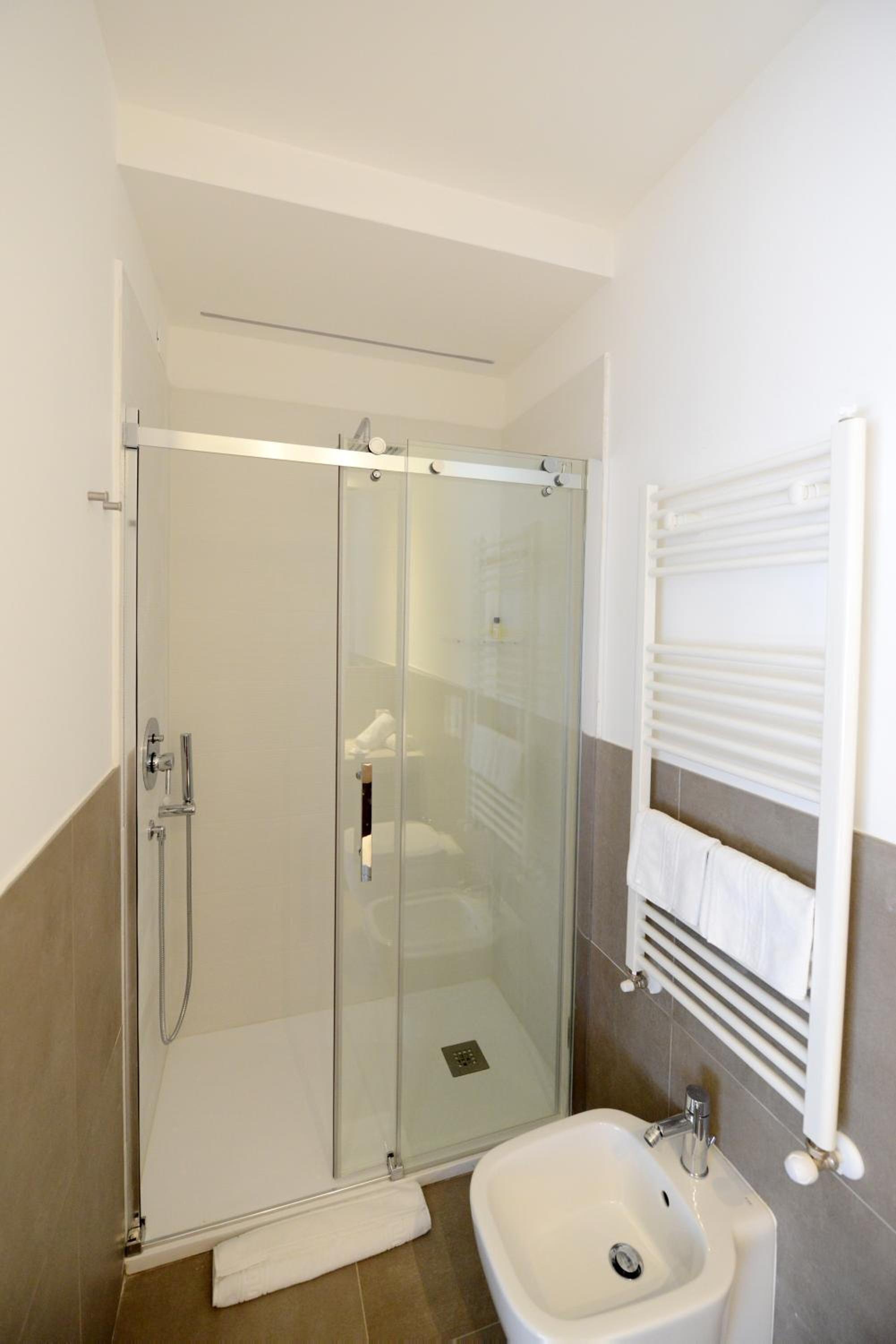 A modern bathroom with a glass-enclosed shower, a white sink, and a towel rack.