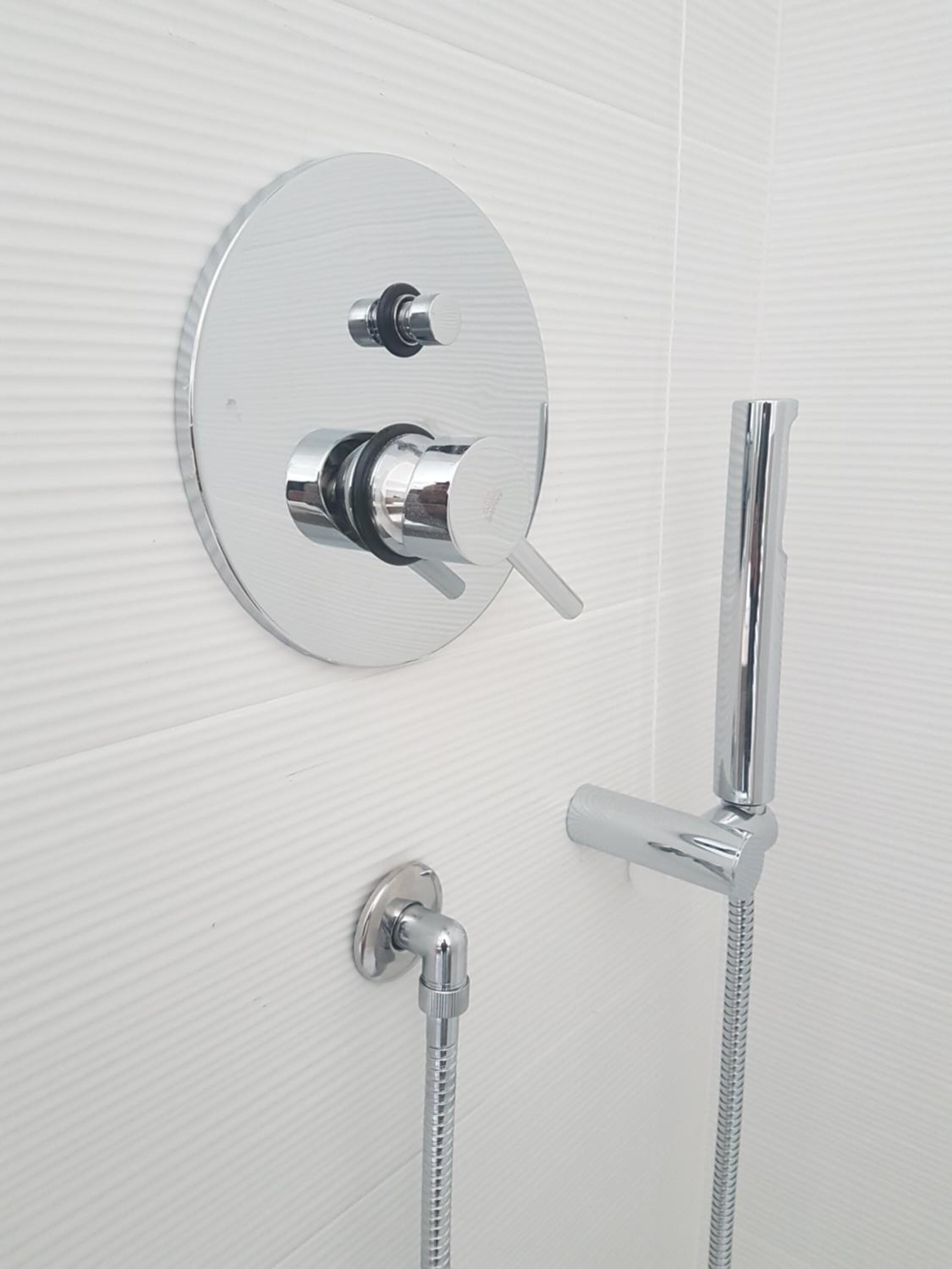 A modern bathroom with a wall-mounted shower control panel, a handheld showerhead, and a flexible hose.