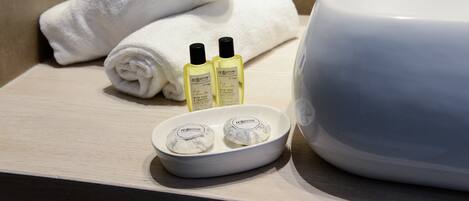 A bathroom with a white sink, two bottles of shampoo, a white towel, and a white bath mat.