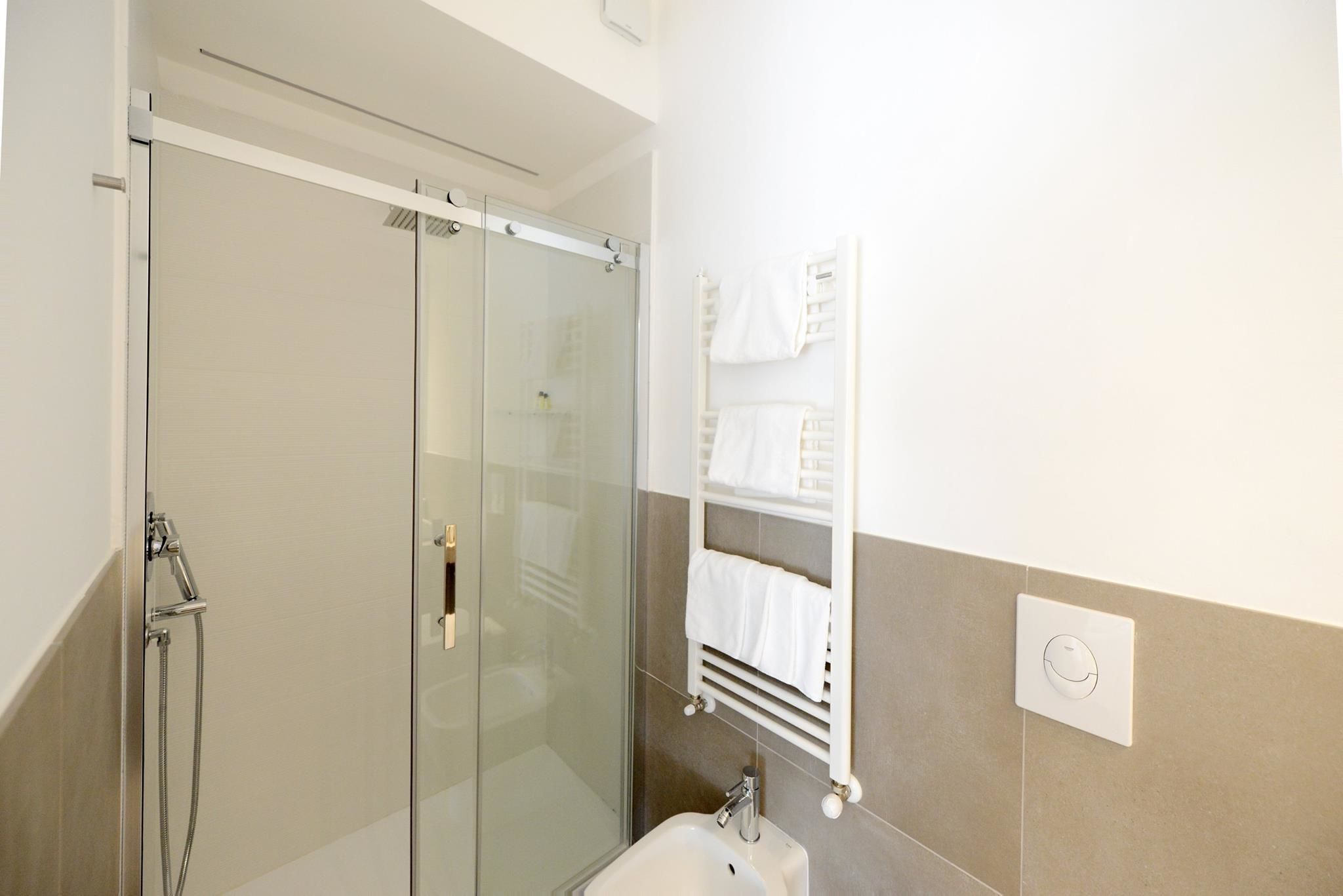 A modern bathroom with a glass shower enclosure, a white sink, and a towel rack with neatly folded towels.