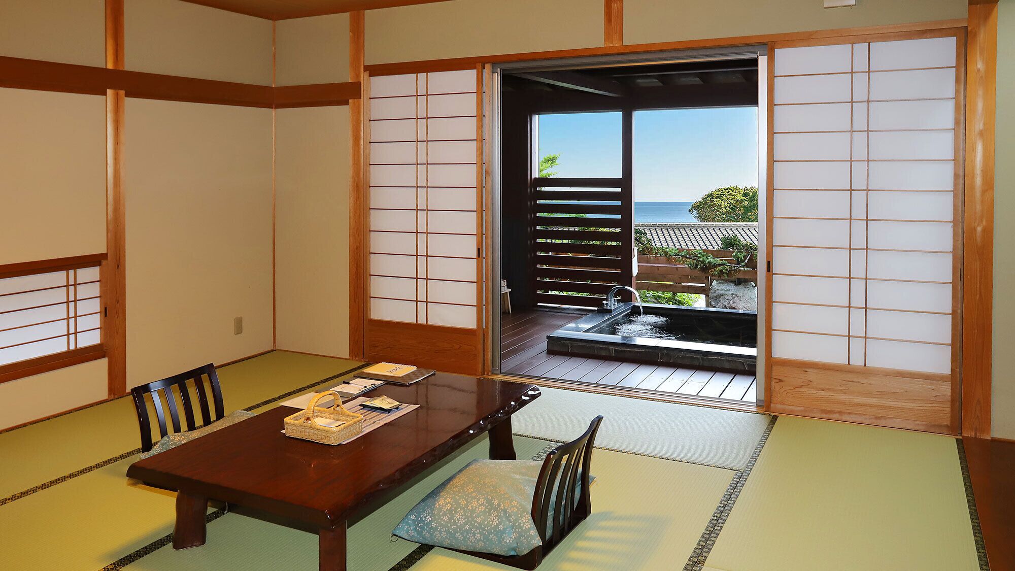 Una habitación japonesa tradicional con suelo de tatami, una mesa baja y puertas correderas que dan a un balcón con vista al mar.
