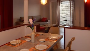 A dining area with a long table set for four, a chandelier with exposed bulbs, and a view of a living room with a sofa and curtains. - ATHENS RIVIERA SEE VIEW  APARTMENT (Pireas)