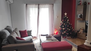 A living room with a sofa, ottoman, and a chessboard. A Christmas tree is visible in the background. - ATHENS RIVIERA SEE VIEW  APARTMENT (Pireas)