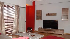 A living room with a sofa, a coffee table, a TV, and a red accent wall. - ATHENS RIVIERA SEE VIEW  APARTMENT (Pireas)