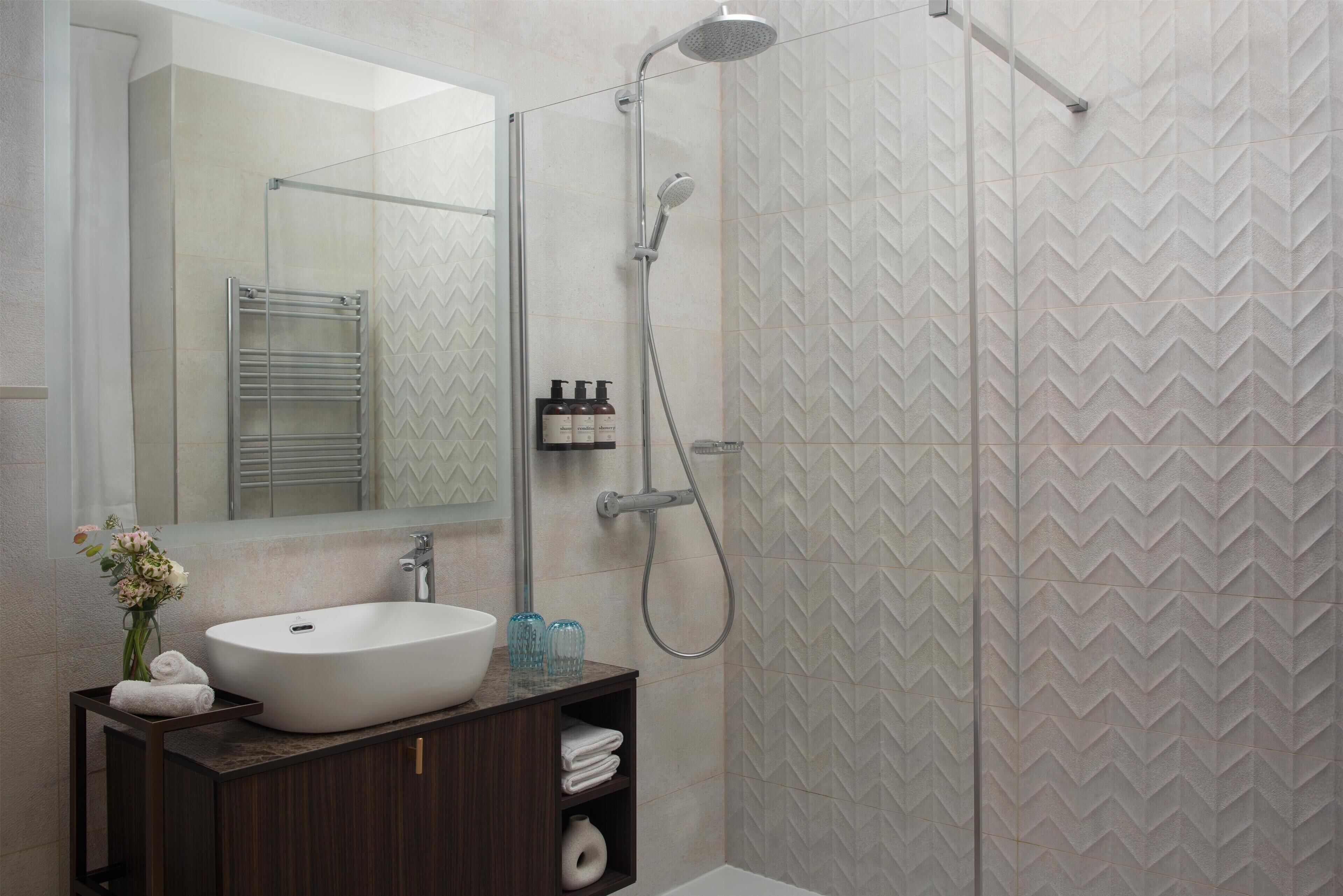Une salle de bain avec un lavabo blanc, un miroir, une douche et des murs carrelés.