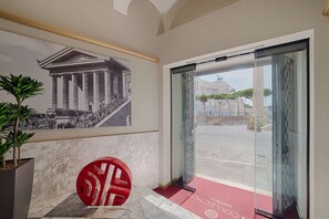A hotel lobby with a marble floor, a large glass door leading outside, and a mural of a classical building.