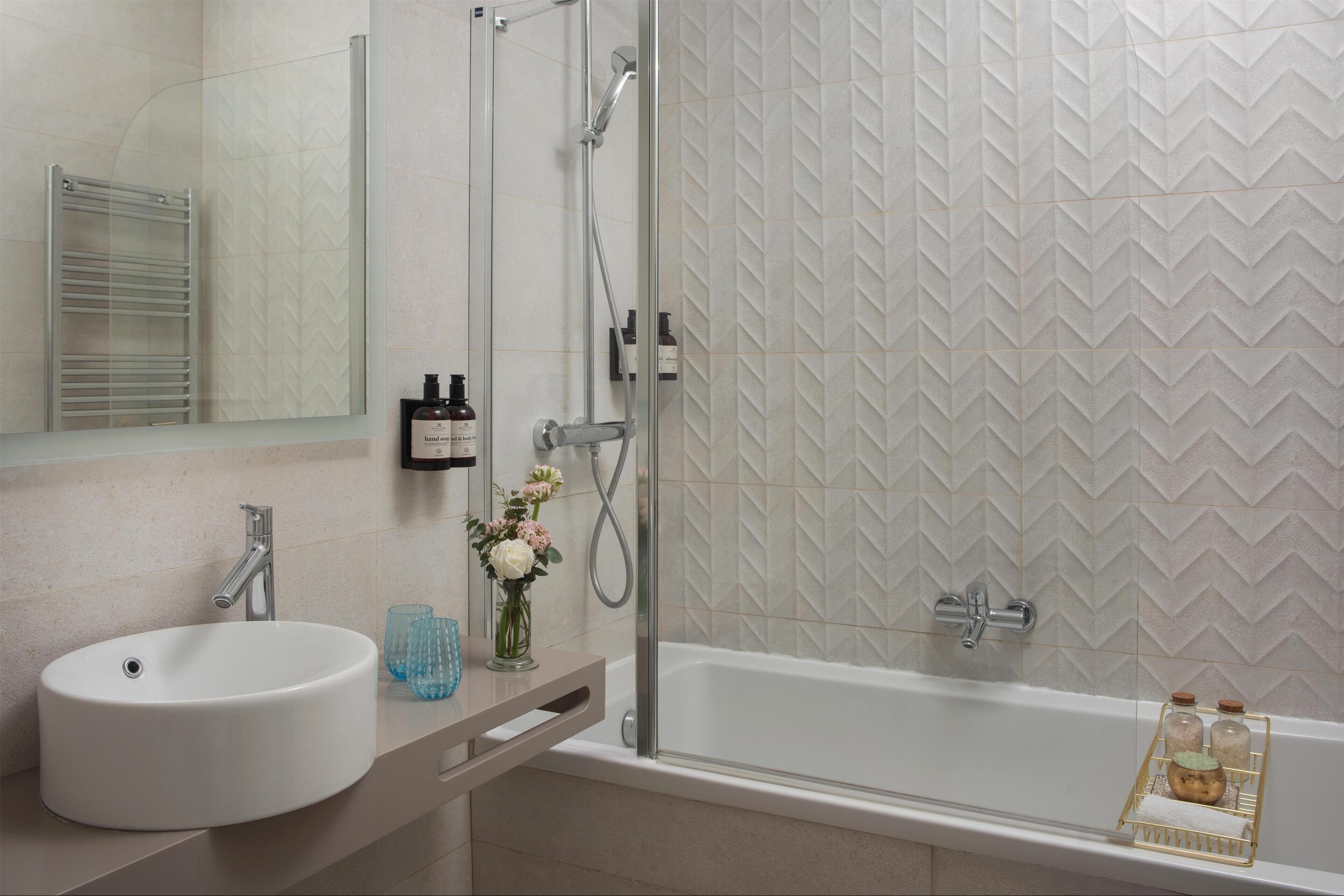 Un baño moderno con lavamanos, espejo, ducha y pared con patrón de espinilla.