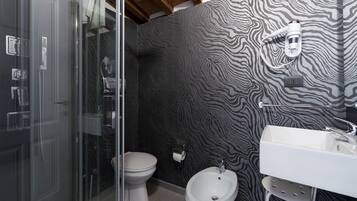 Un bagno con box doccia in vetro, un water bianco, un bidet e un lavandino bianco con portasci.