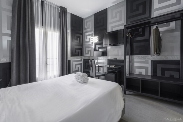 A modern hotel room with a large bed, a desk, and a TV.