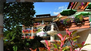 Un pati amb una fontana, envoltat de balcons amb jardineres florals i un arbre.