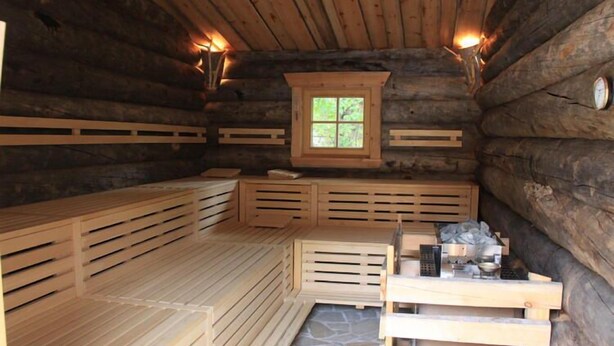 Sauna de fusta tipus cabana amb seients de fusta i sòl de pedra.