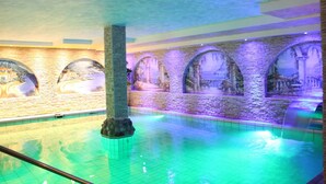Una piscina interior amb paret de pedra i finestres d'arc.