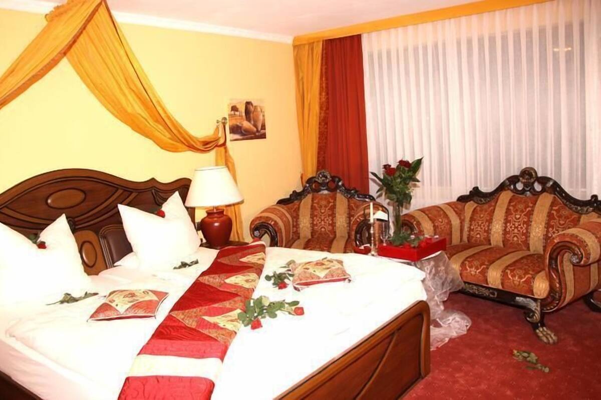 Una habitación de hotel con cama, sofá, lámpara y ventana con cortinas.
