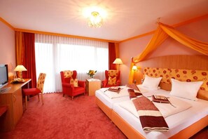 Een hotelkamer met een groot bed, twee stoelen, een bureau en een televisie.