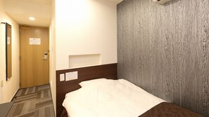 Habitación de hotel con puerta de madera, cama con almohada blanca, repisa montada en la pared y pared con textura.
