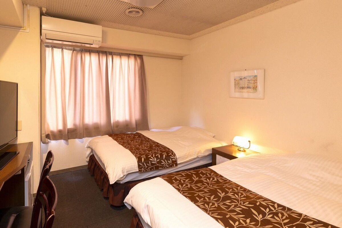 Une chambre d’hôtel avec deux lits, une télévision, un appareil de climatisation et une fenêtre avec des rideaux.