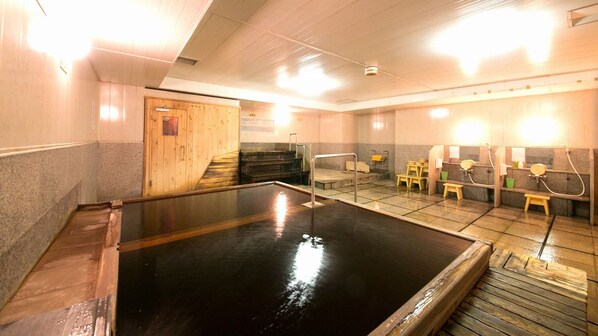 A sauna room with a large heated pool, wooden benches, and a wooden door.