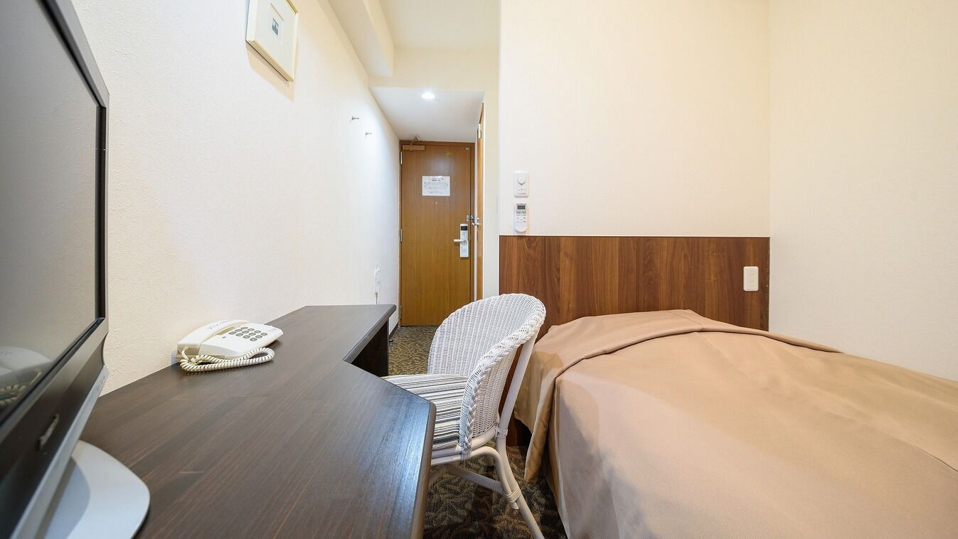 A small hotel room with a desk, a telephone, a chair, and a bed.