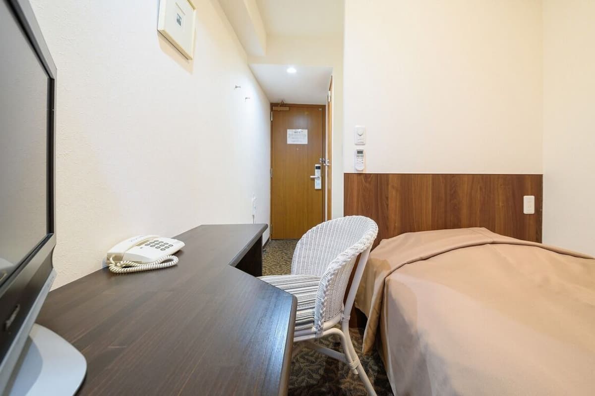A small hotel room with a desk, a telephone, a chair, and a bed.