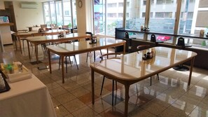 A clean, well-lit room with multiple tables and chairs, large windows offering a view of the city, and a modern design. - New Gloria Oita Hotel (Oita)