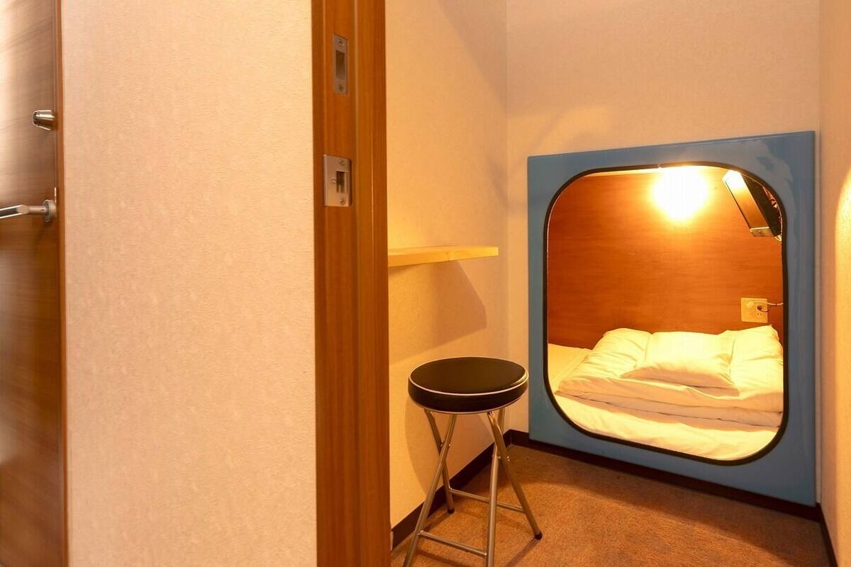 A small room with a bed, a stool, and a door.