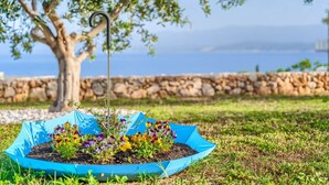 Un jardin avec un pot à fleurs bleu en forme de parasol, contenant des fleurs aux couleurs vives, un arbre et un mur de pierre en arrière-plan.