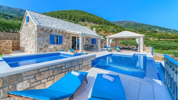 Un espace piscine agrémenté de murs en pierre, de chaises longues bleues et d’un coin salon abrité.