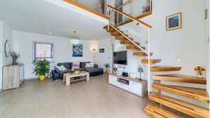 Un salon moderne avec un escalier, un ensemble de canapés, une table basse et un téléviseur.