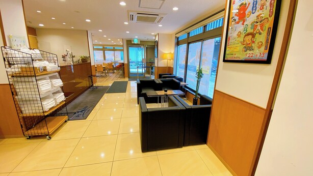 A hotel lobby with a reception desk, seating area, and a display of folded towels. - REX INN Namba (Osaka)