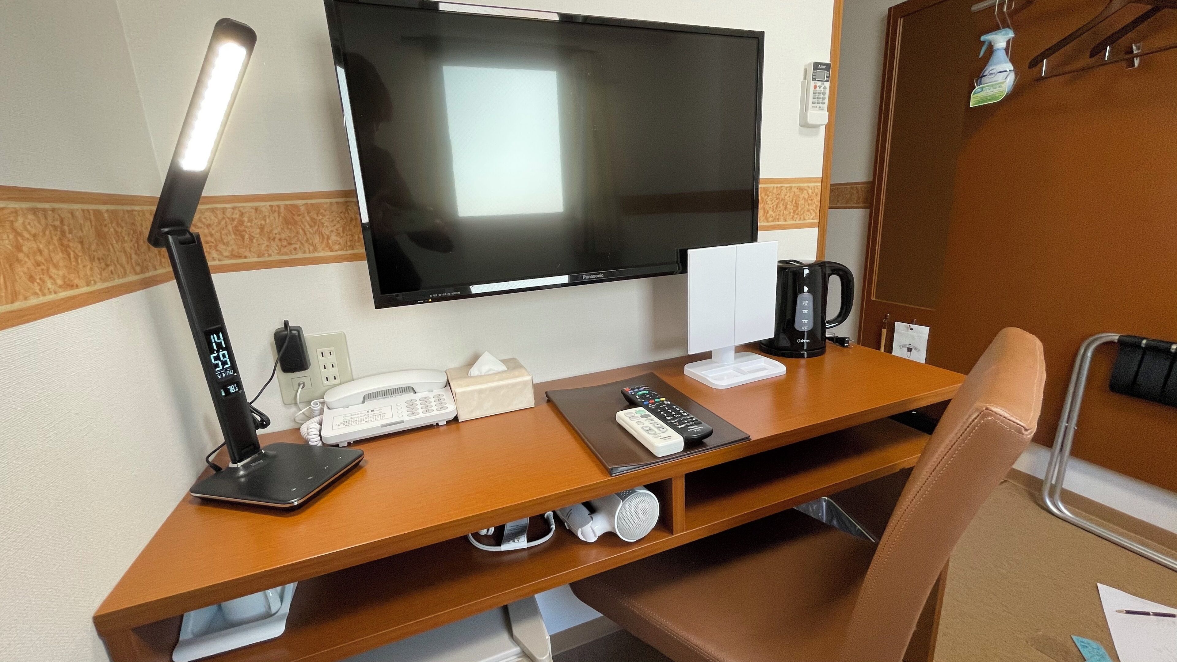A hotel room with a TV, desk, lamp, phone, remote controls, and a coffee maker.