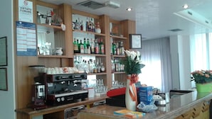 A bar area with a coffee machine, shelves with bottles, and a vase with flowers. - Hotel Nuova Doel (Chioggia)