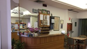 A reception area with a wooden counter, a clock, framed photos, and a menu board. - Hotel Nuova Doel (Chioggia)
