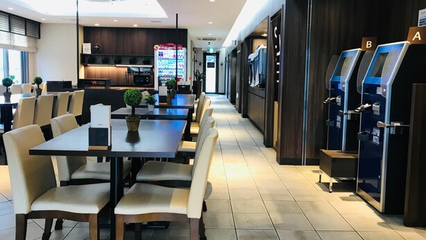 Un vestíbulo de hotel con una larga recepción, un área de estar y una kitchenette al fondo.