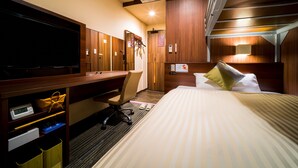 Una habitación de hotel con cama, escritorio con silla, televisión y aire acondicionado.