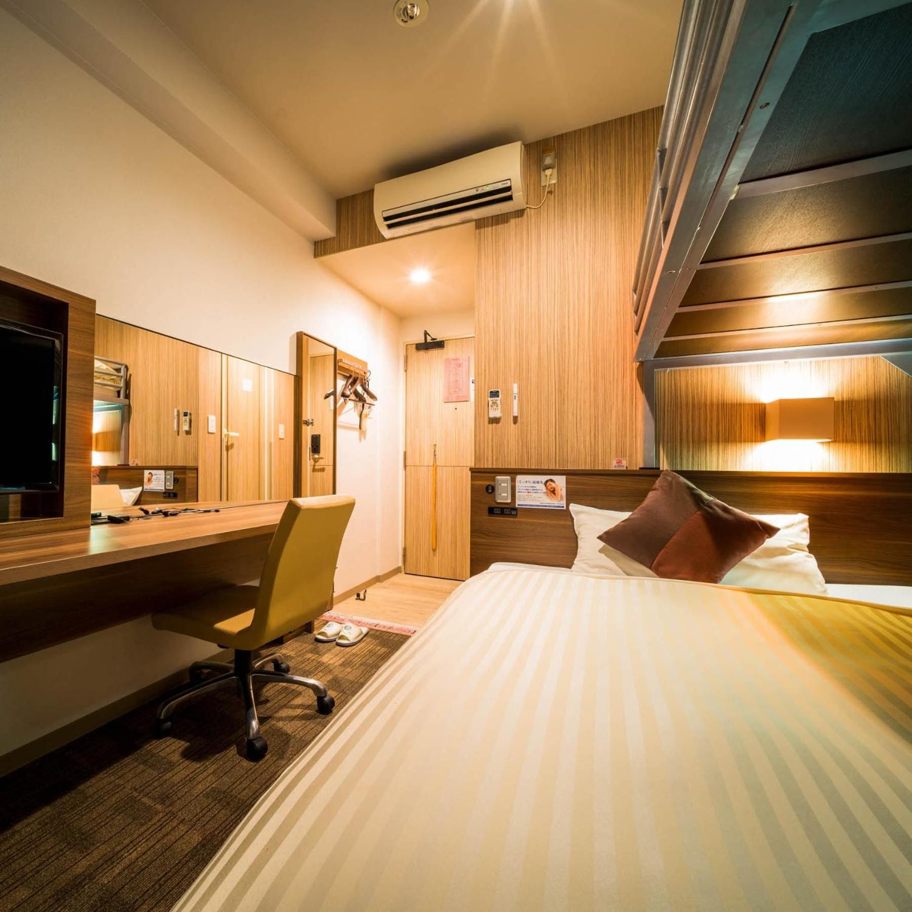 Ein Hotelzimmer mit Bett, Schreibtisch, Stuhl, Klimaanlage und einer Holzwand.