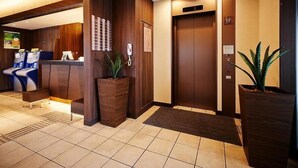 Un vestíbulo de hotel con una recepción, dos ascensores y plantas en macetas.