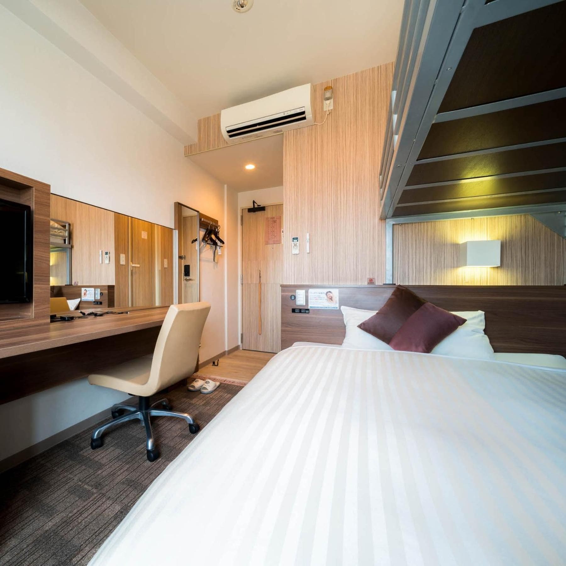 Een hotelkamer met een bed, een bureau, een stoel, een spiegel en een airconditioner.