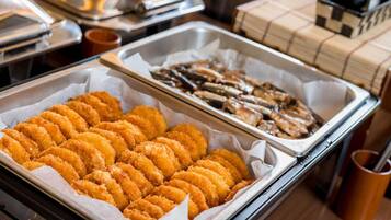 A buffet setup with trays of breaded and fried food items, a coffee machine, and a stack of napkins.