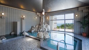 A modern indoor pool with a stone waterfall feature, tiled walls, and a view of the outdoors. - Resort Club Iseshima (Shima)