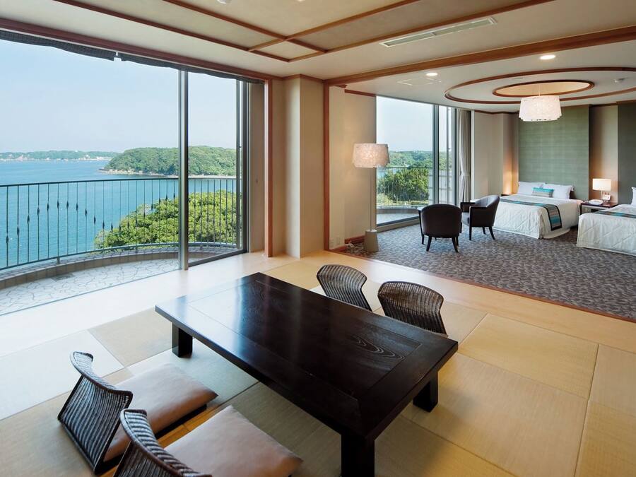 A hotel room with a large balcony, a bed, a desk, and a view of the sea.