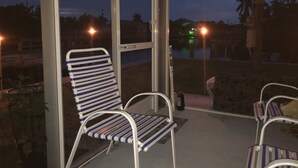 A covered outdoor seating area with metal chairs and a glass partition.