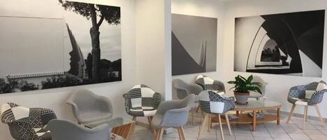 Un interior moderno con una zona de estar que incluye sillas grises y con estampado, una mesa redonda de madera y una planta en maceta.