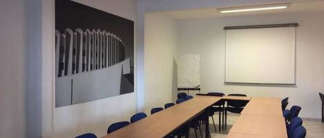 A conference room with a long table, blue chairs, a projector screen, and a whiteboard.