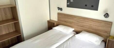 A single bed with a wooden headboard, a small bedside table, and a wall-mounted picture.