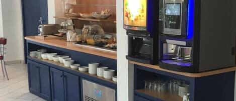 A self-service beverage station with a coffee machine, a TV screen, and a variety of cups and glasses.