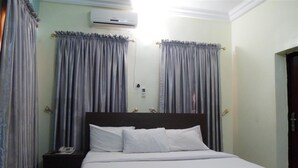 A hotel room with a bed, curtains, an air conditioning unit, and a nightstand with a phone. - Orange Groove Hotel (Kaduna)