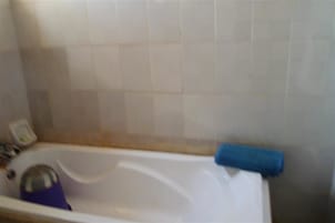 Um banheiro com uma banheira, uma toalha azul e um objeto roxo na borda.