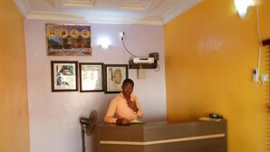 A reception area with a reception desk, framed pictures on the wall, and a poster above the desk. - Orange Groove Hotel (Kaduna)