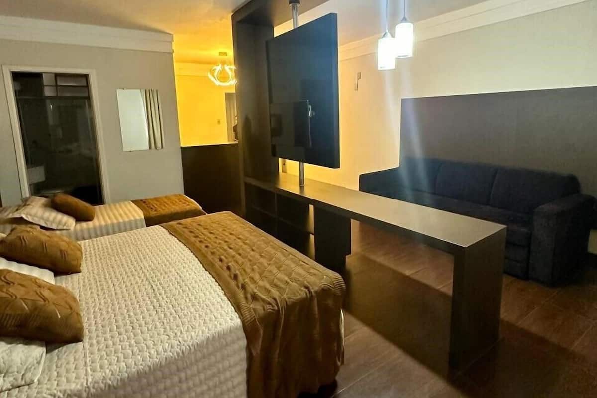Ein modernes Hotelzimmer mit zwei Betten, einer Couch, einem Fernseher und einem Schreibtisch.